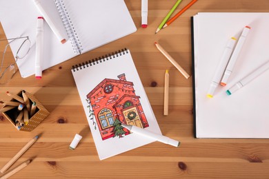 Photo of Sketchbook with beautiful drawing of house and pencils on wooden table, flat lay