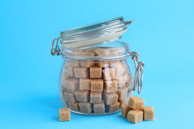 Photo of Brown sugar cubes in glass jar on light blue background, closeup