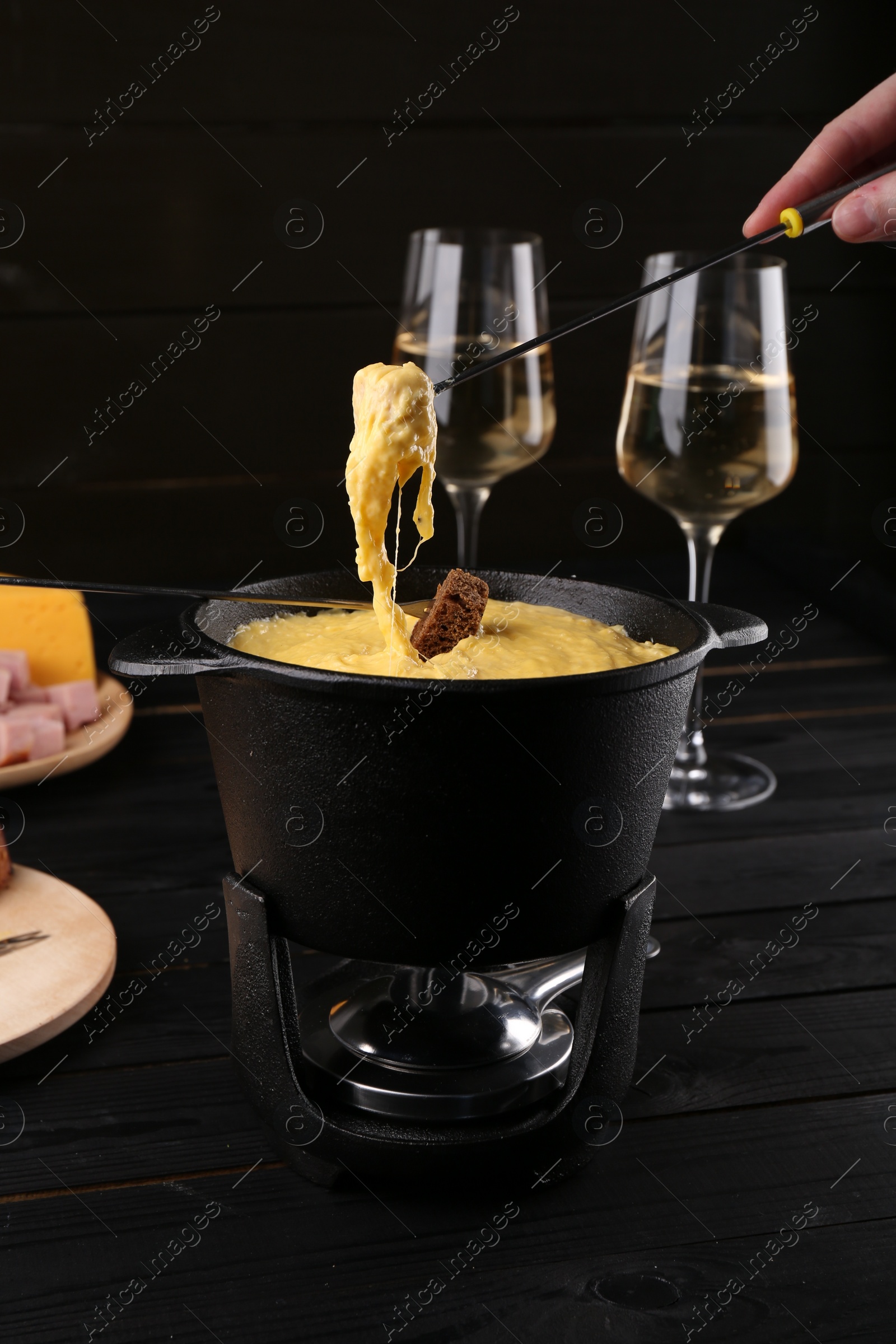 Photo of Woman dipping pieces of ham and bread into fondue pot with melted cheese at table, closeup