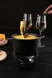 Photo of Woman dipping pieces of ham and bread into fondue pot with melted cheese at table, closeup