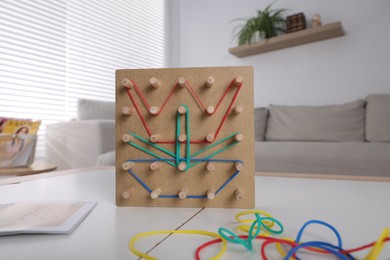 Photo of Wooden geoboard with flower made of rubber bands on white table in room. Motor skills development