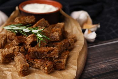 Crispy rusks with rosemary and sauce on wooden table, closeup. Space for text