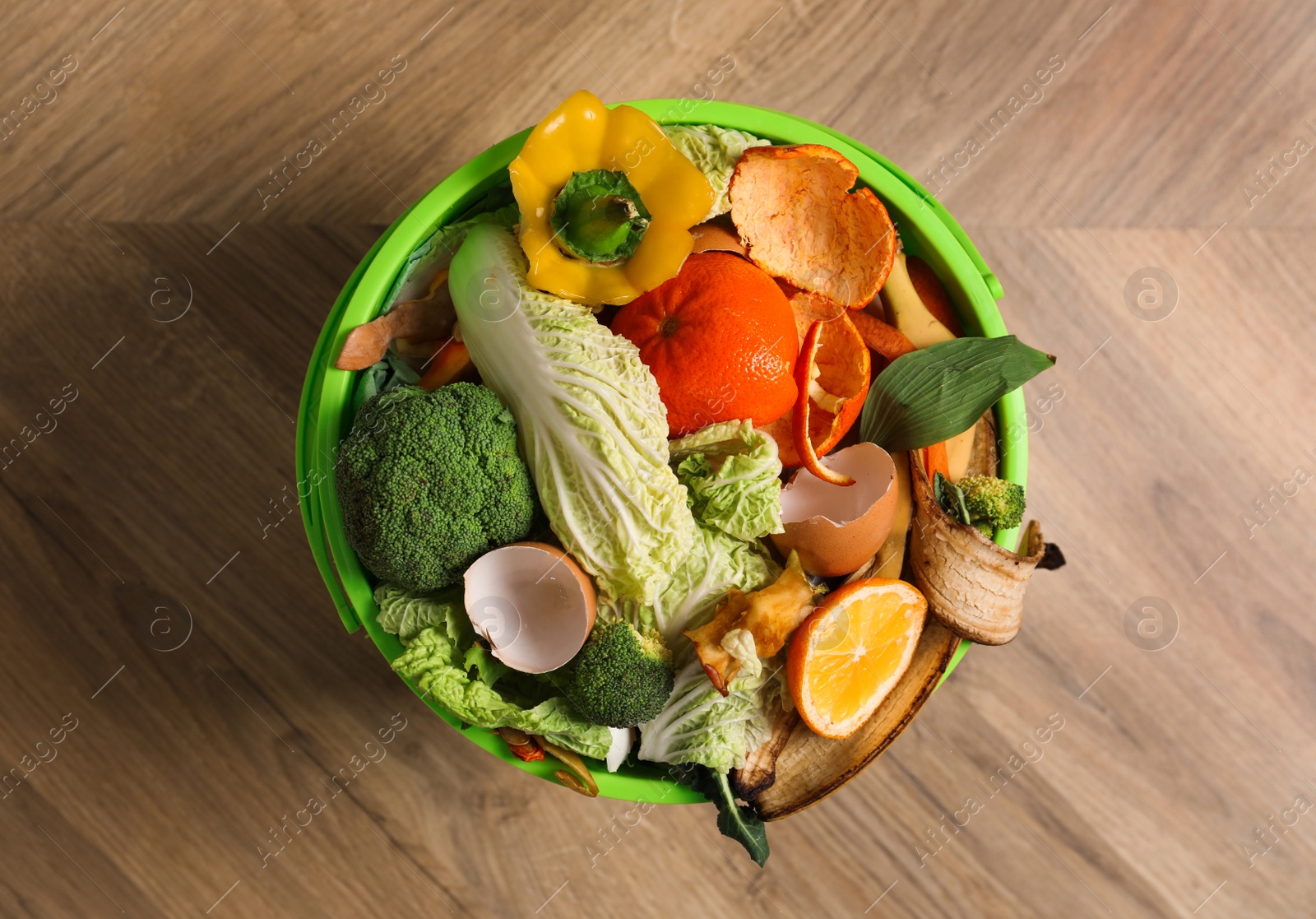 Photo of Trash bin with organic waste for composting on wooden background, top view