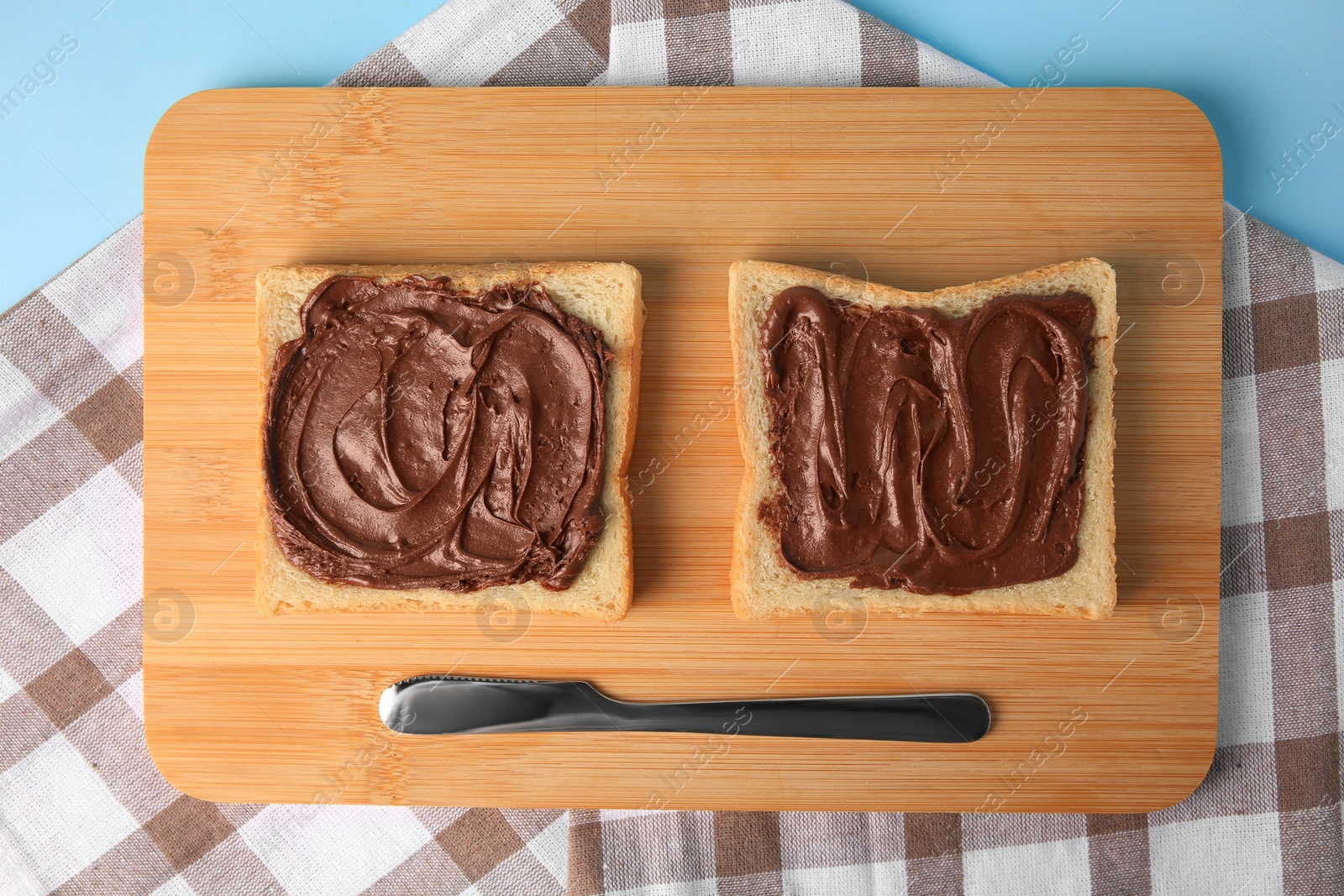 Photo of Tasty toasts with chocolate paste served on light blue background, top view