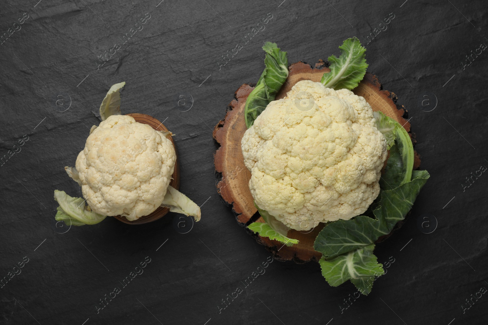 Photo of Fresh raw cauliflower cabbages on black table, flat lay