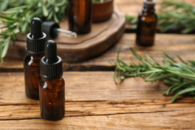 Bottles of rosemary essential oil on wooden table. Space for text