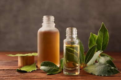 Bottles of bay essential oil and fresh leaves on wooden table