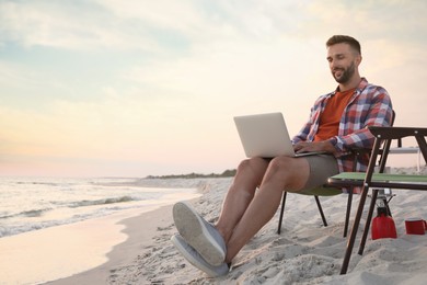 Photo of Man using laptop in camping chair on sandy beach