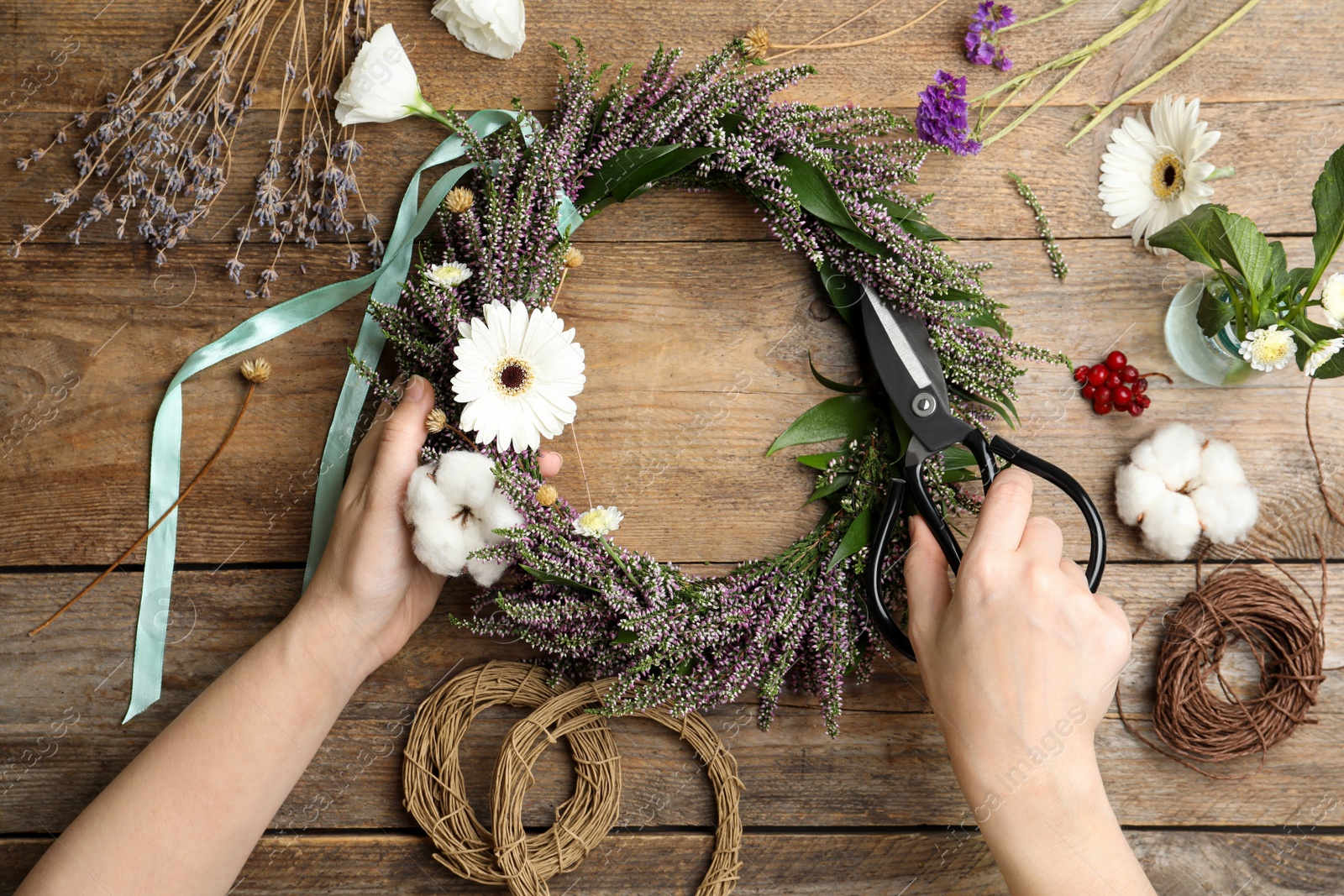 Photo of Florist making beautiful autumnal wreath with heather flowers at wooden table, top view