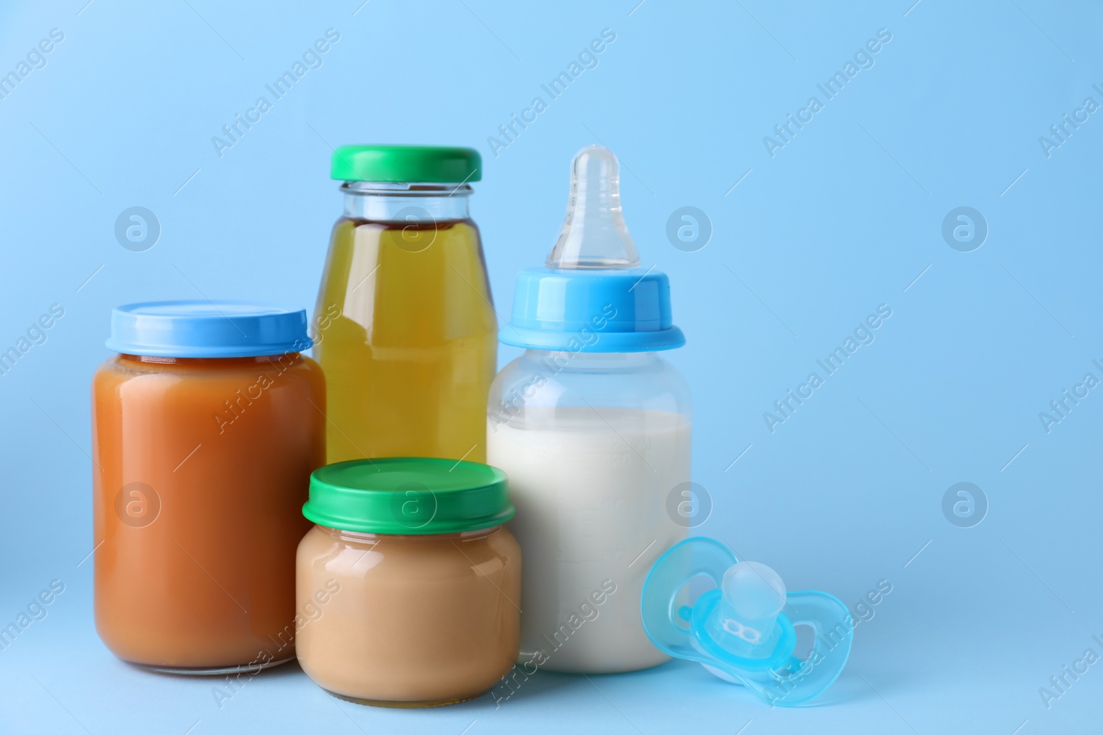 Photo of Healthy baby food, juice, milk and pacifier on light blue background