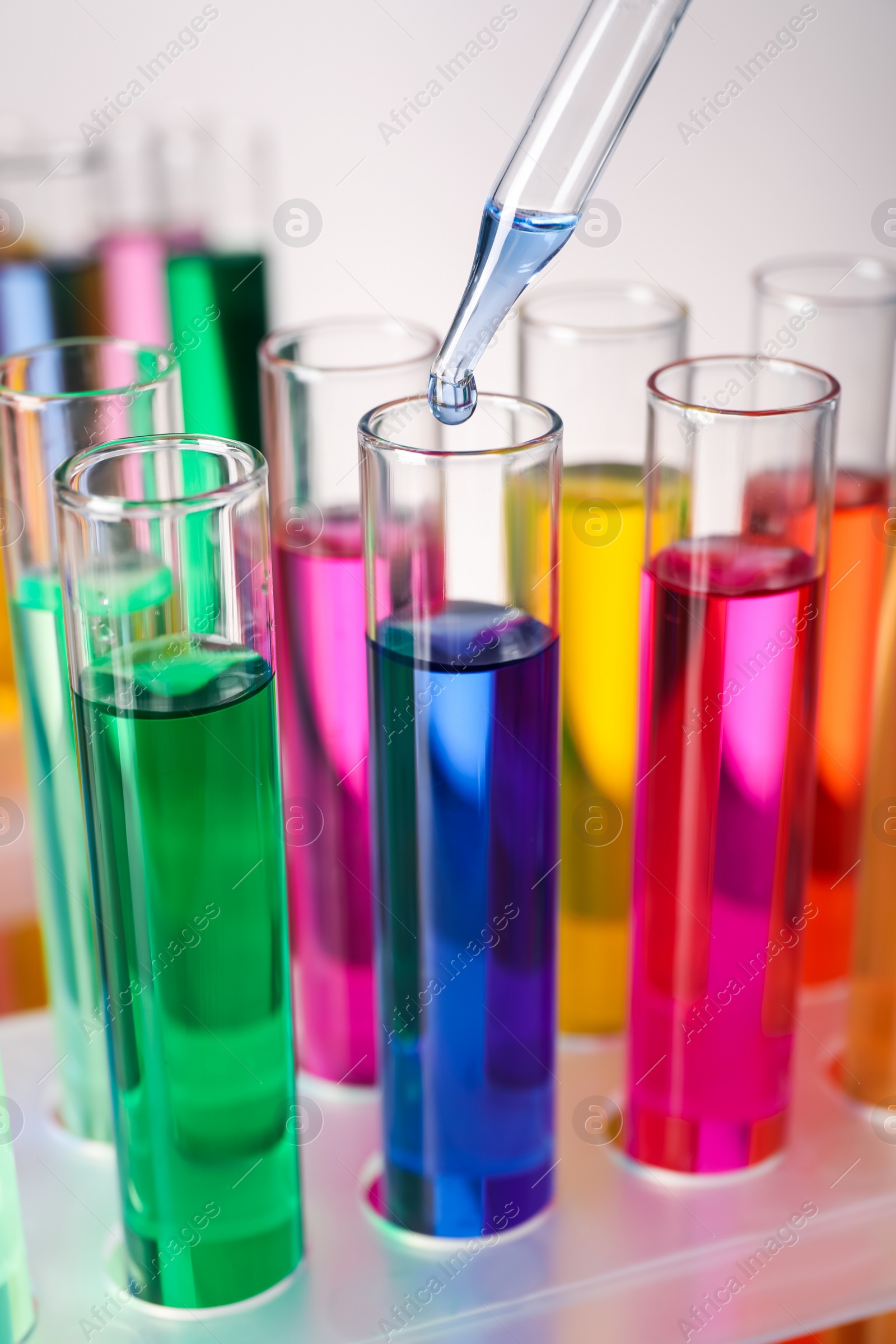 Photo of Dripping liquid from pipette into test tube on grey background, closeup