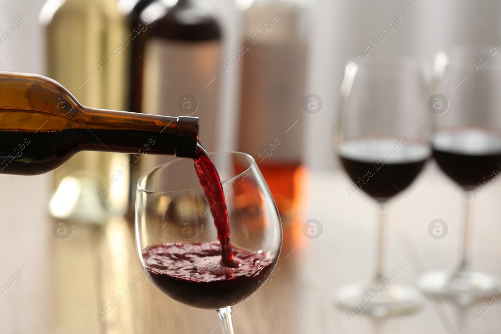 Photo of Pouring red wine from bottle into glass on blurred background, closeup. Space for text