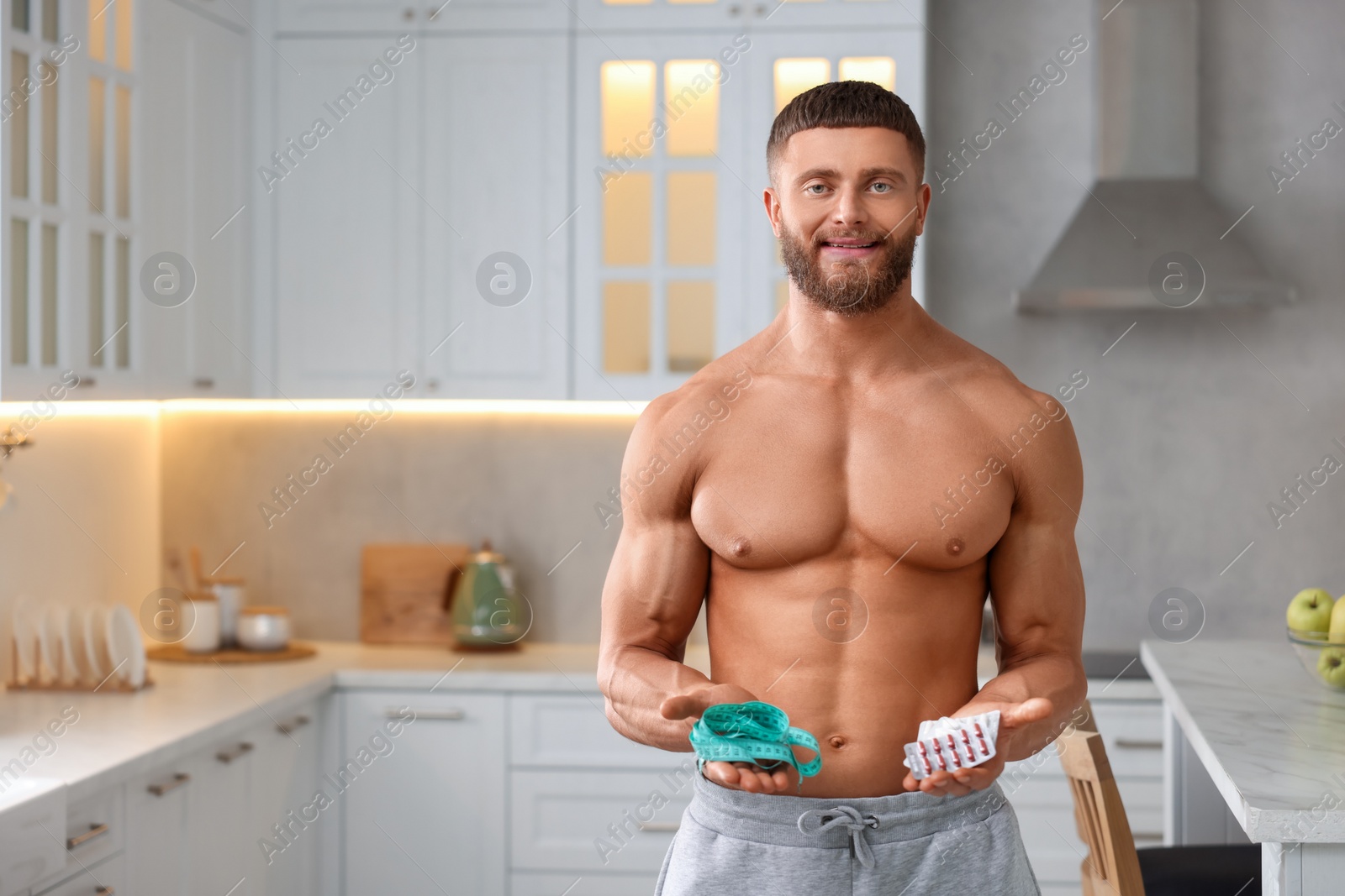 Photo of Athletic young man with measuring tape and supplements in kitchen, space for text. Weight loss