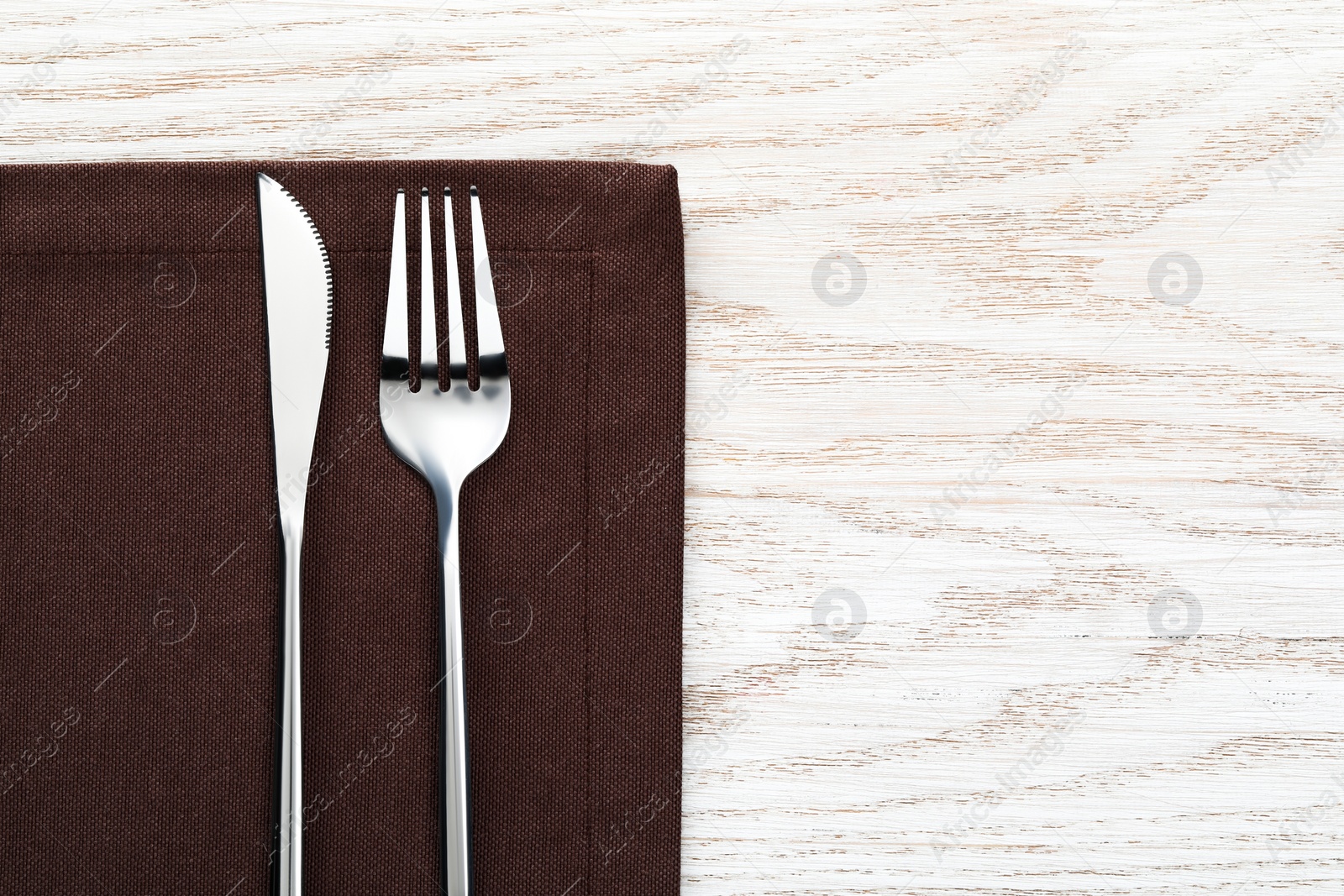 Photo of Fork, knife and napkin on white wooden table, top view with space for text. Stylish shiny cutlery set