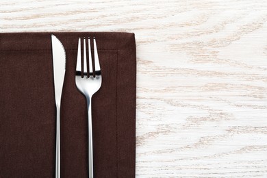 Photo of Fork, knife and napkin on white wooden table, top view with space for text. Stylish shiny cutlery set