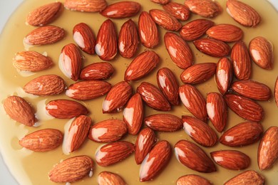 Tasty almond nuts with honey as background, above view