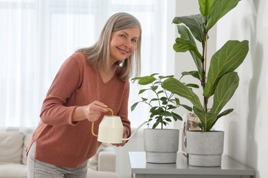 Photo of Senior woman watering beautiful potted houseplants at home