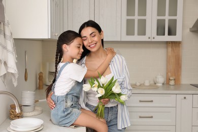 Photo of Little daughter congratulating her mom in kitchen at home. Happy Mother's Day