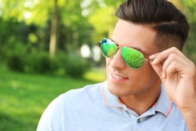 Handsome man wearing stylish sunglasses in park. Space for text