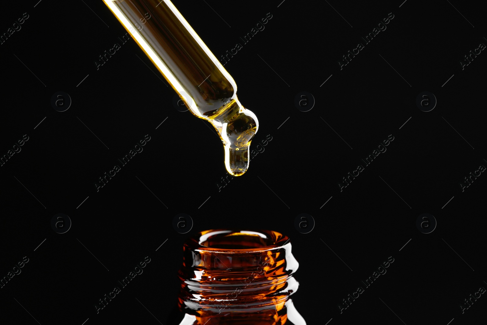 Photo of Dripping tincture from pipette into bottle on black background, closeup