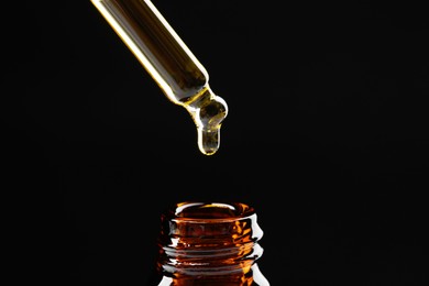 Photo of Dripping tincture from pipette into bottle on black background, closeup