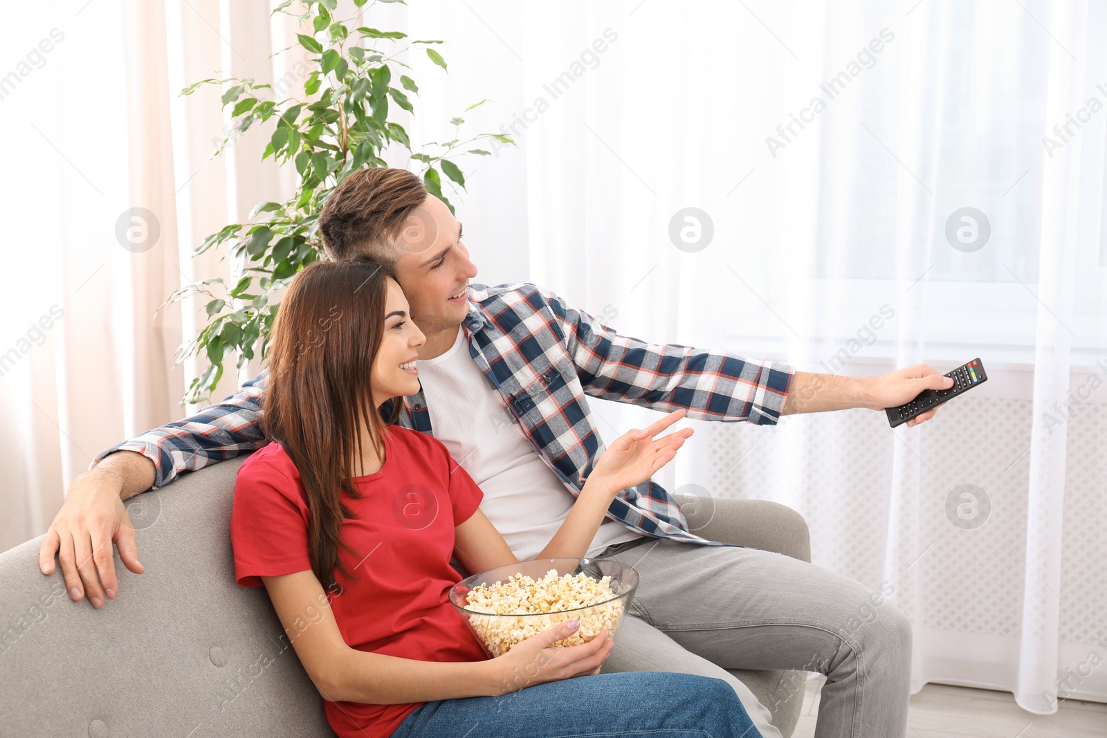 Photo of Happy young couple watching TV on sofa at home