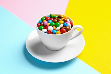 Delicious bright glazed candies in cup on color background