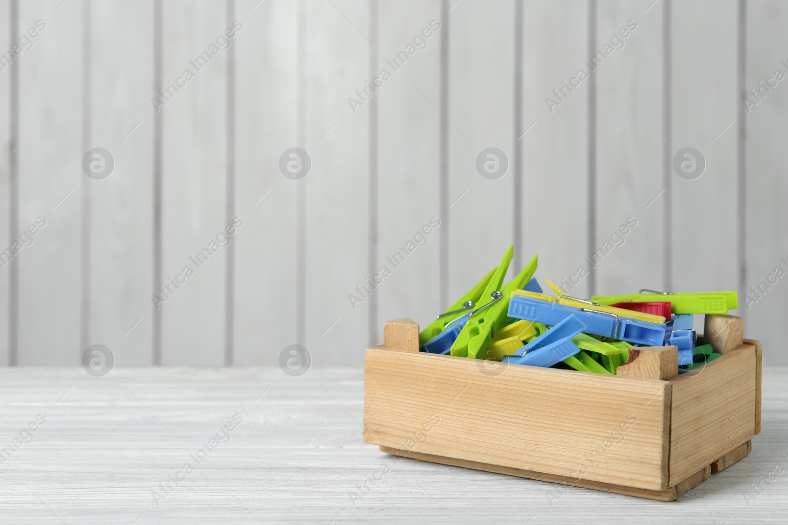 Photo of Crate with colorful clothespins on white wooden table. Space for text