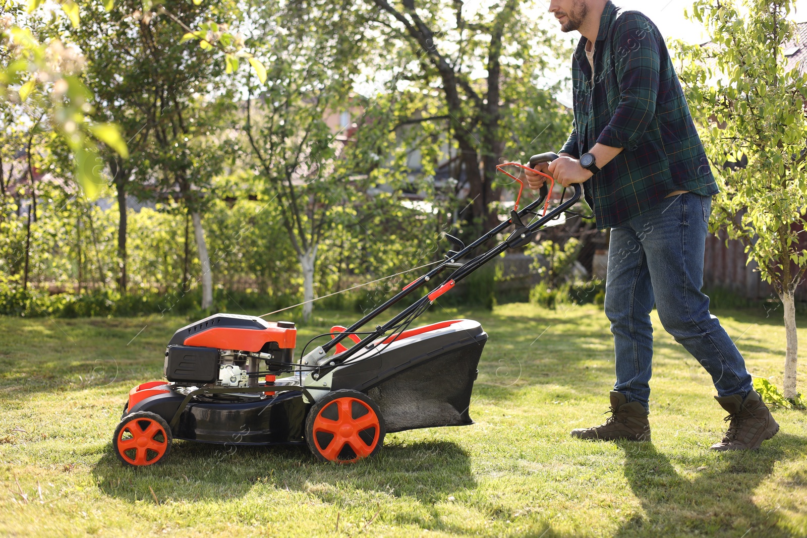 Photo of Man cutting green grass with lawn mower in garden, closeup