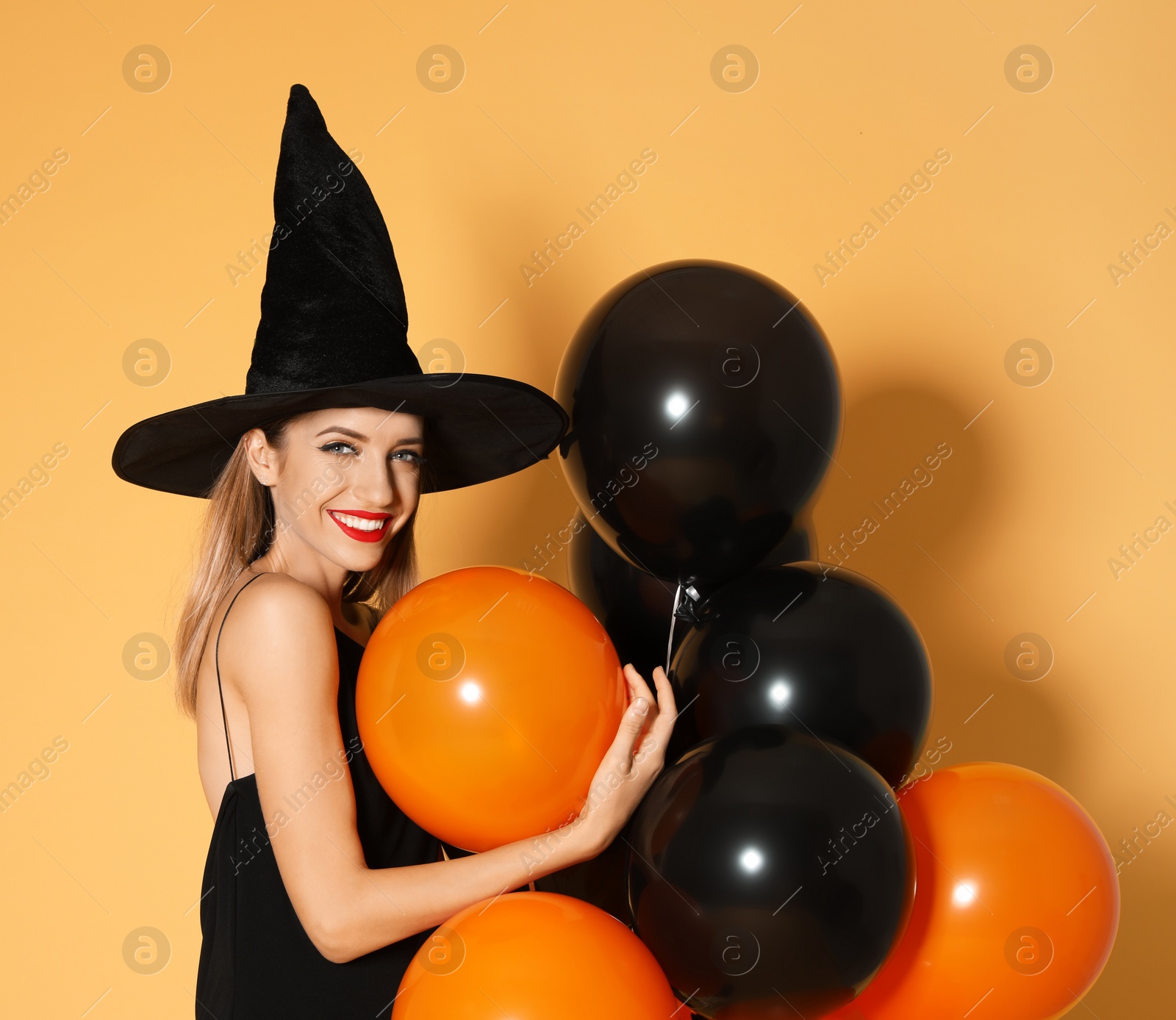 Photo of Beautiful woman wearing witch costume with balloons for Halloween party on yellow background