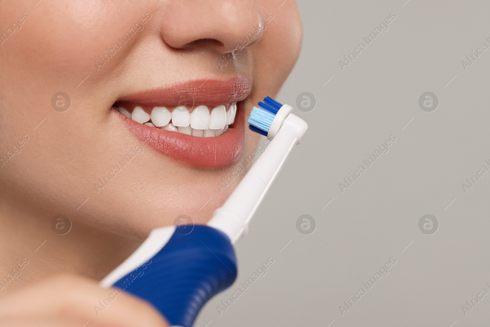 Photo of Woman brushing her teeth with electric toothbrush on light grey background, closeup. Space for text