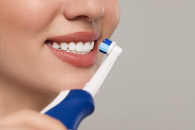 Woman brushing her teeth with electric toothbrush on light grey background, closeup. Space for text