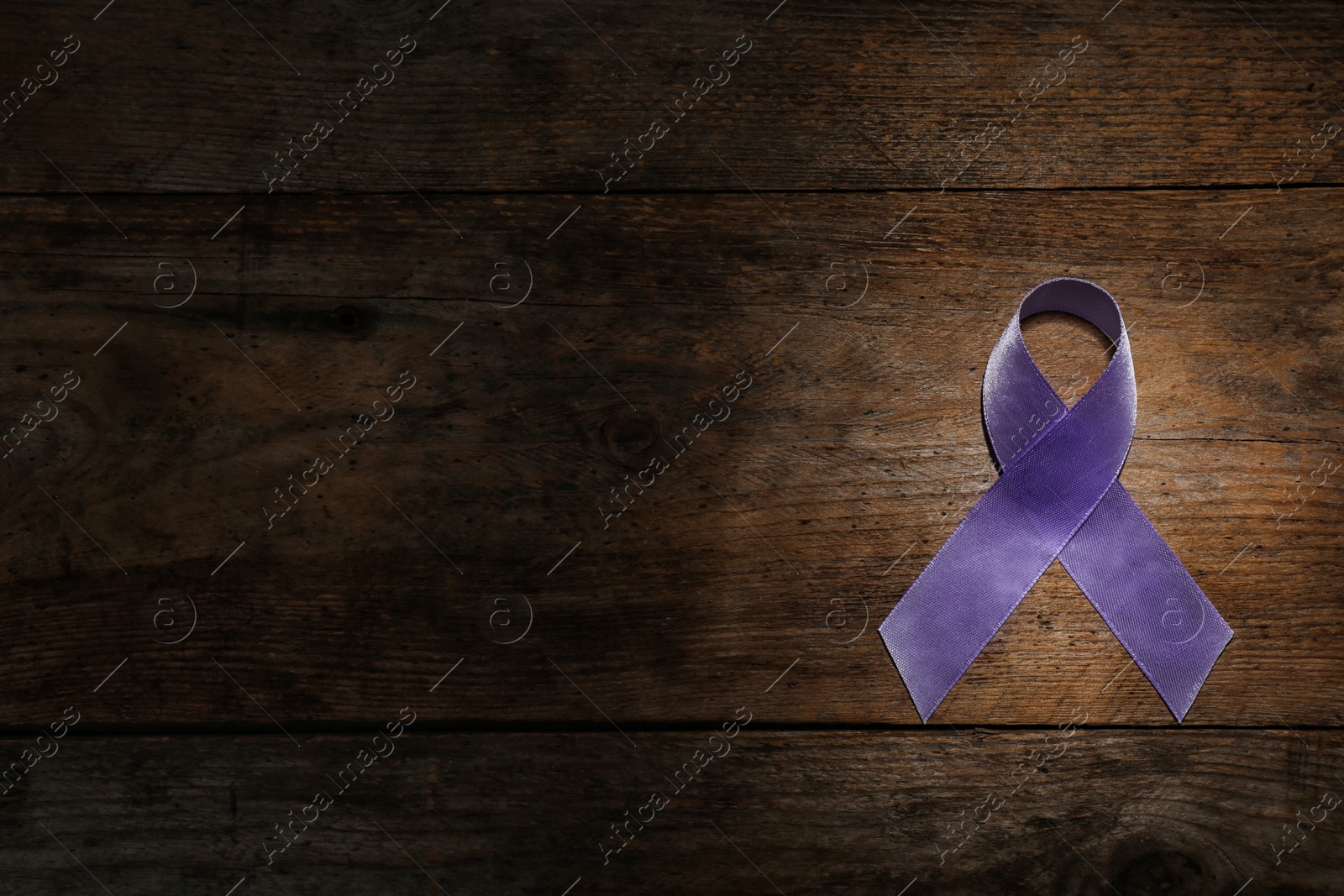 Photo of Purple ribbon on brown wooden background, top view with space for text. Domestic violence awareness
