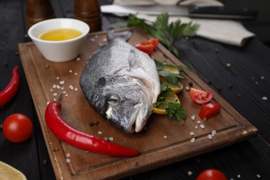 Photo of Fresh raw dorado fish with lemon, spices and tomatoes on black wooden table