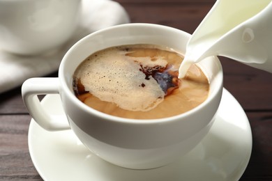 Photo of Pouring milk into cup of hot coffee on wooden table, closeup