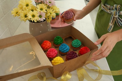 Woman with box of delicious colorful cupcakes at white table, closeup