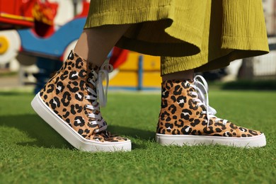 Woman wearing sneakers with leopard print on green grass outdoors, closeup