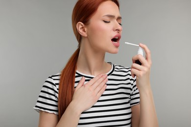 Young woman using throat spray on grey background