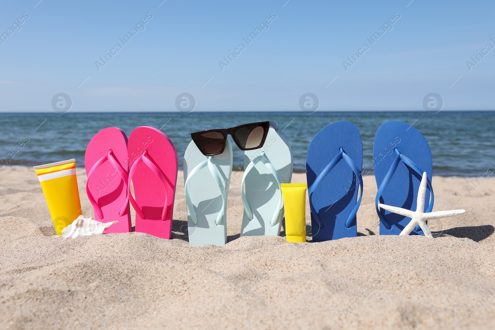 Photo of Stylish colorful flip flops with sunglasses and sunscreens on beach sand