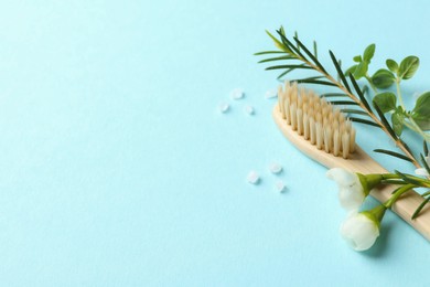 Photo of Bamboo toothbrush, beautiful flowers, sea salt and herbs on light blue background, closeup. Space for text