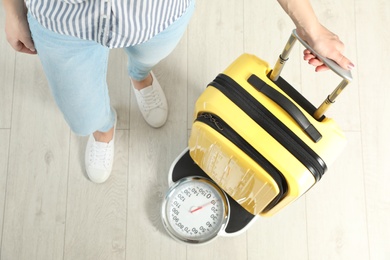Photo of Woman weighing modern suitcase indoors, top view