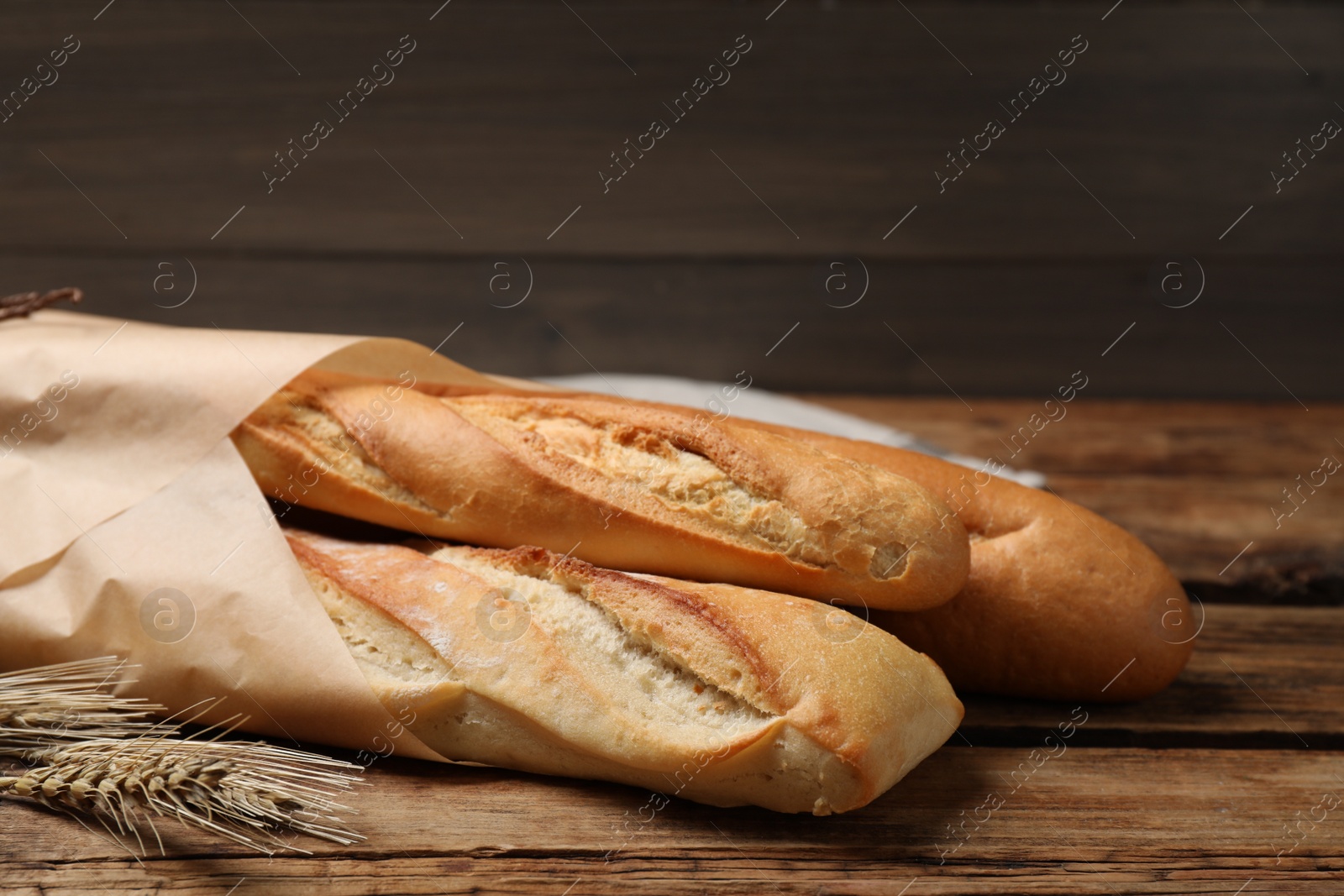 Photo of Fresh tasty baguettes and spikelets on wooden table, closeup