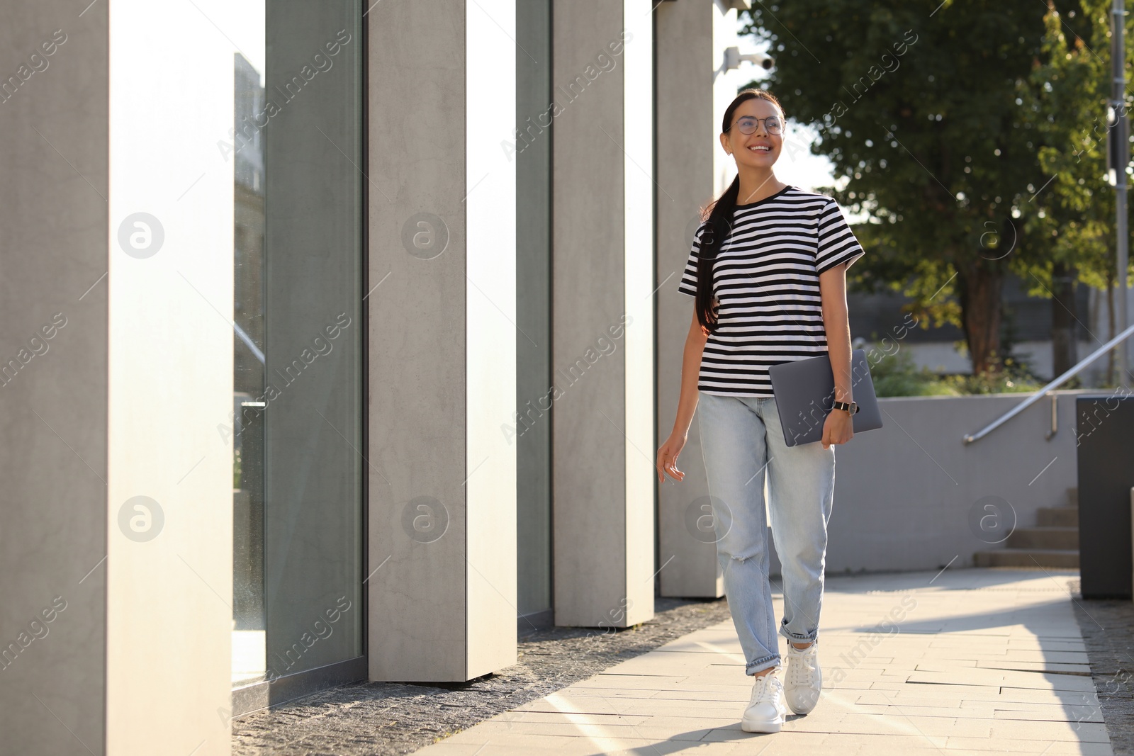 Photo of Happy young woman holding modern laptop outdoors. Space for text