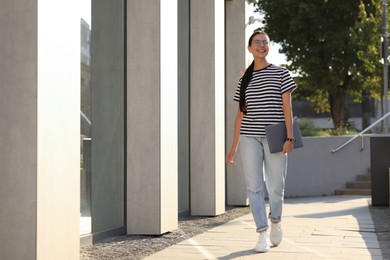 Happy young woman holding modern laptop outdoors. Space for text