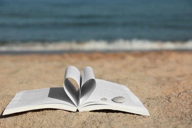 Photo of Open book with pages folded in heart shape on sandy beach near sea