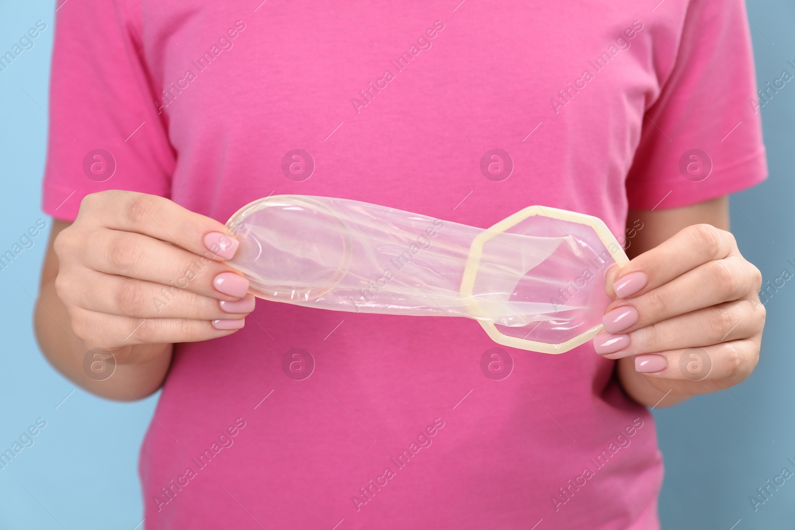 Photo of Woman with unrolled female condom on light blue background, closeup. Safe sex