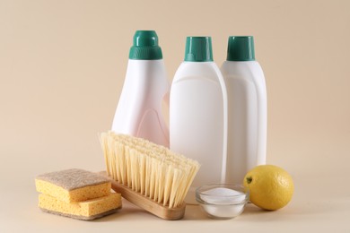 Bottles of cleaning product, sponges, brush, lemon and baking soda on beige background