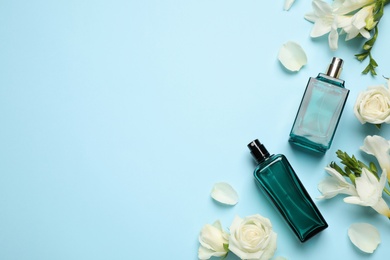 Photo of Flat lay composition with different perfume bottles and flowers on light blue background, space for text