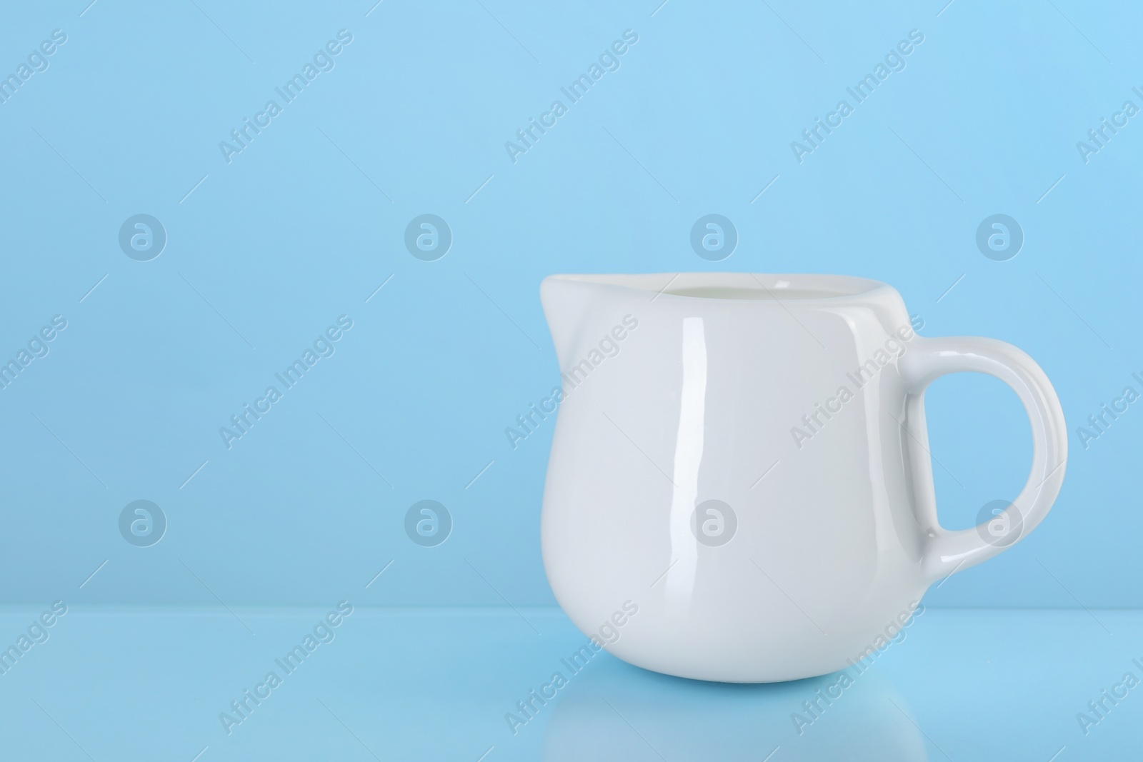 Photo of Jug of fresh milk on light blue background, space for text