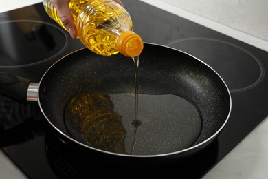 Photo of Woman pouring cooking oil into frying pan on stove, closeup